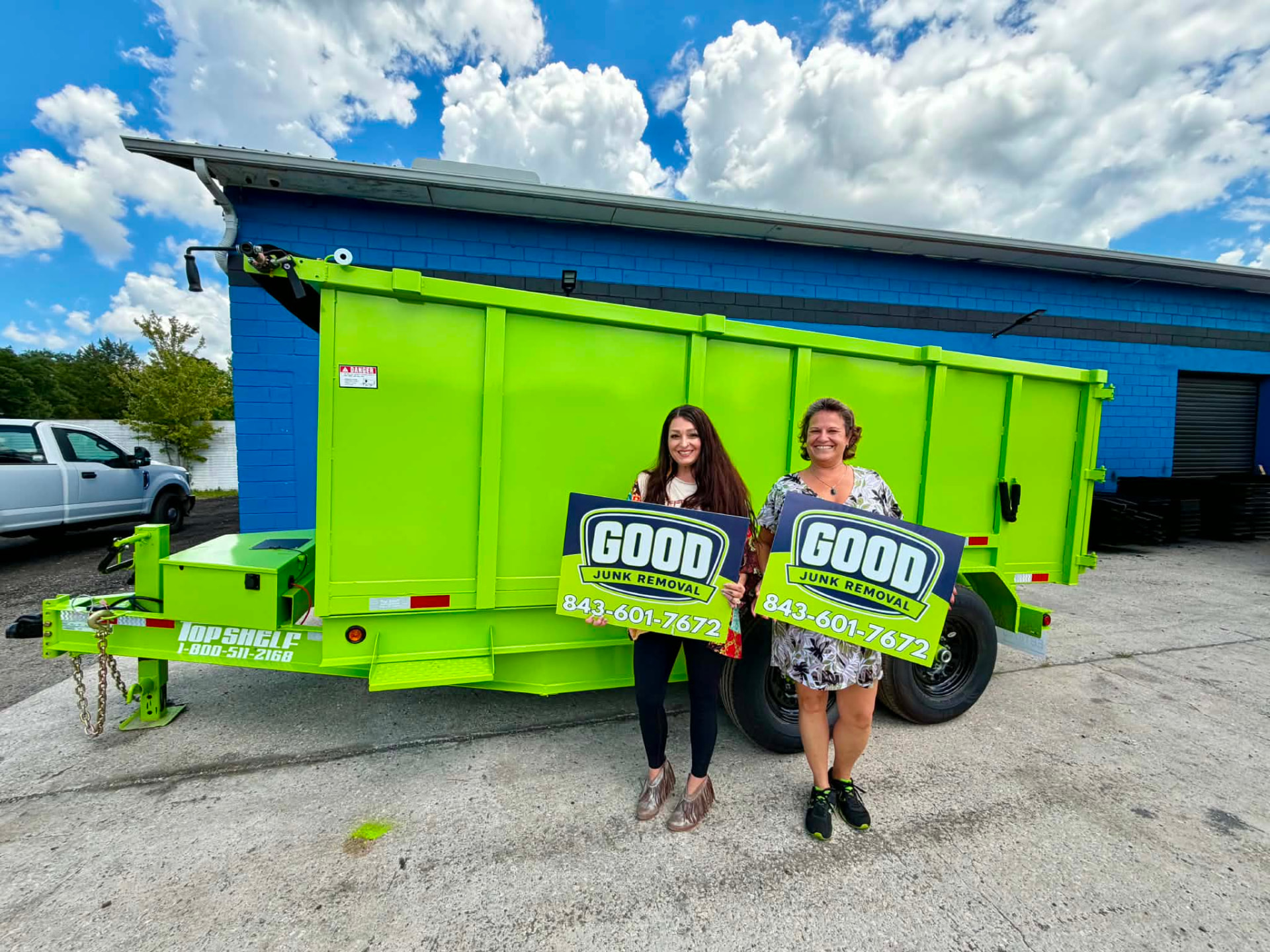 GOOD JUNK team holding signs in front of a green dump trailer